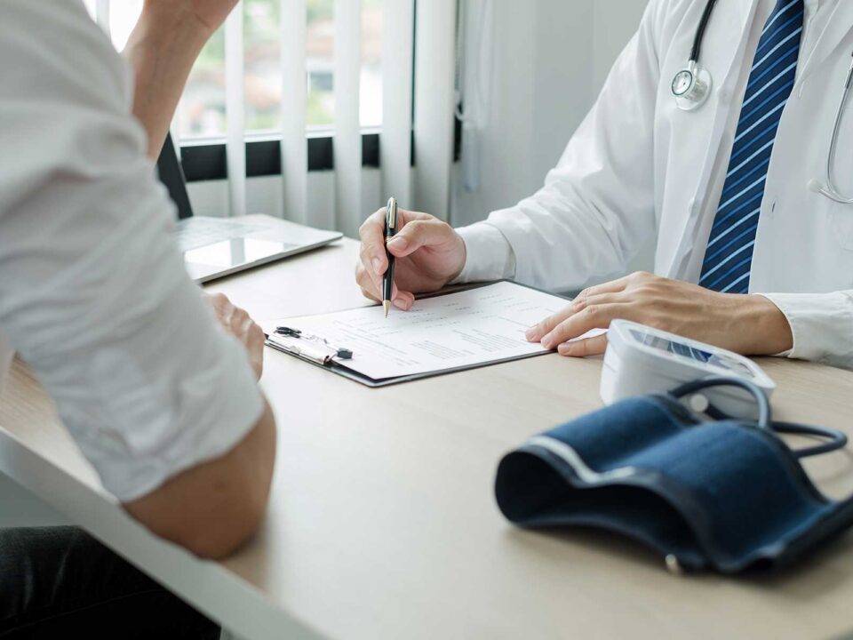 Doctor writes notes on paper while talking to client at desk