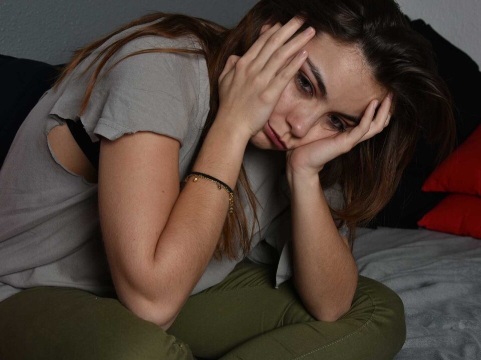 Woman sits on bed holding head in agony, exhibiting symptoms of heroin abuse