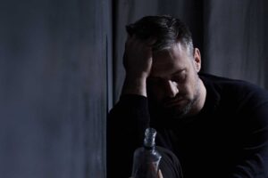 Man rests head on hands, feeling symptoms of alcohol abuse