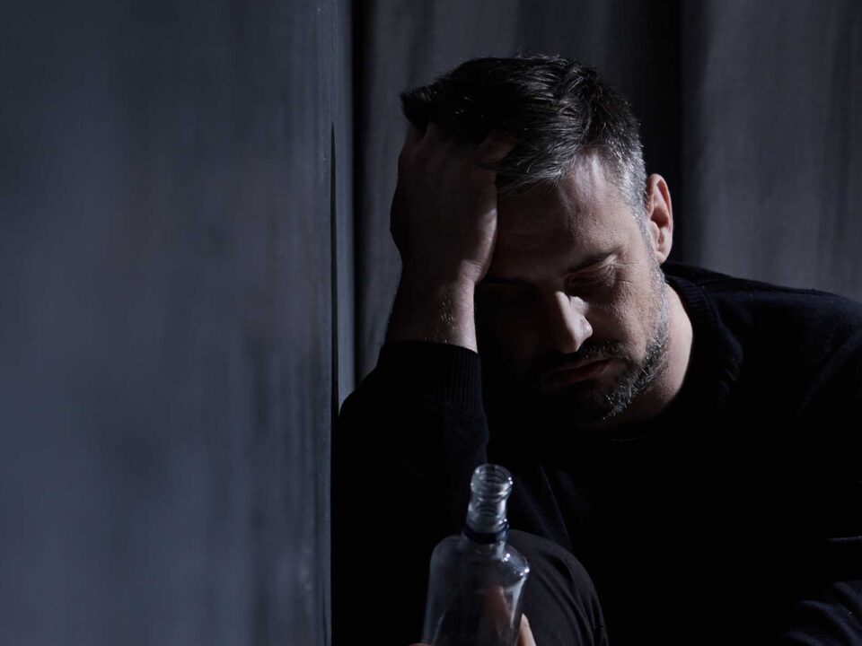 Man rests head on hands, feeling symptoms of alcohol abuse