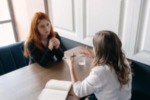 Two people sit at table and discuss prescription drug rehab programs