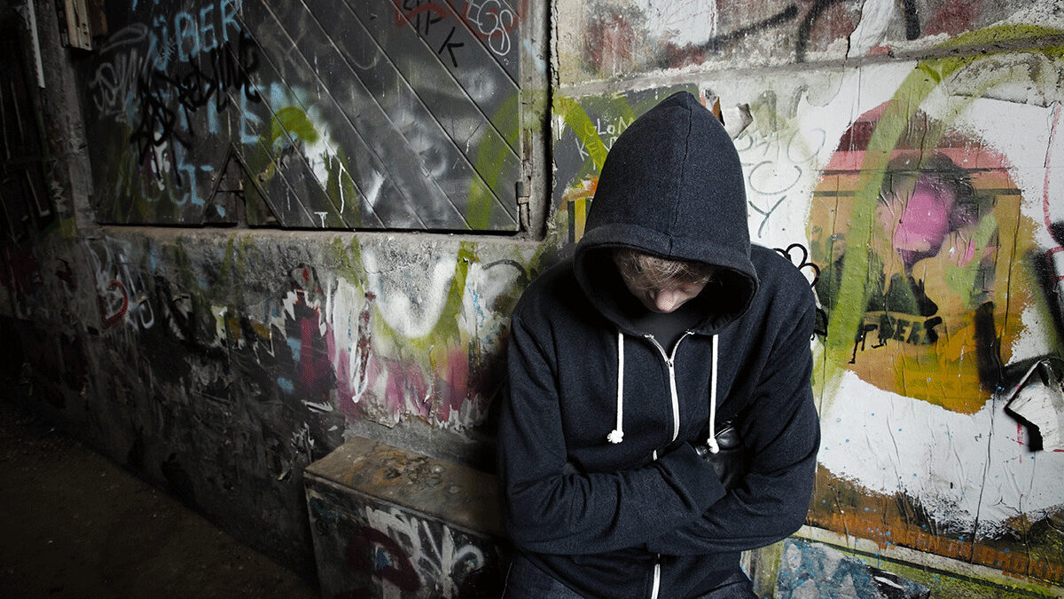 Man in hoodie leans against wall as he wonders what meth addiction looks like
