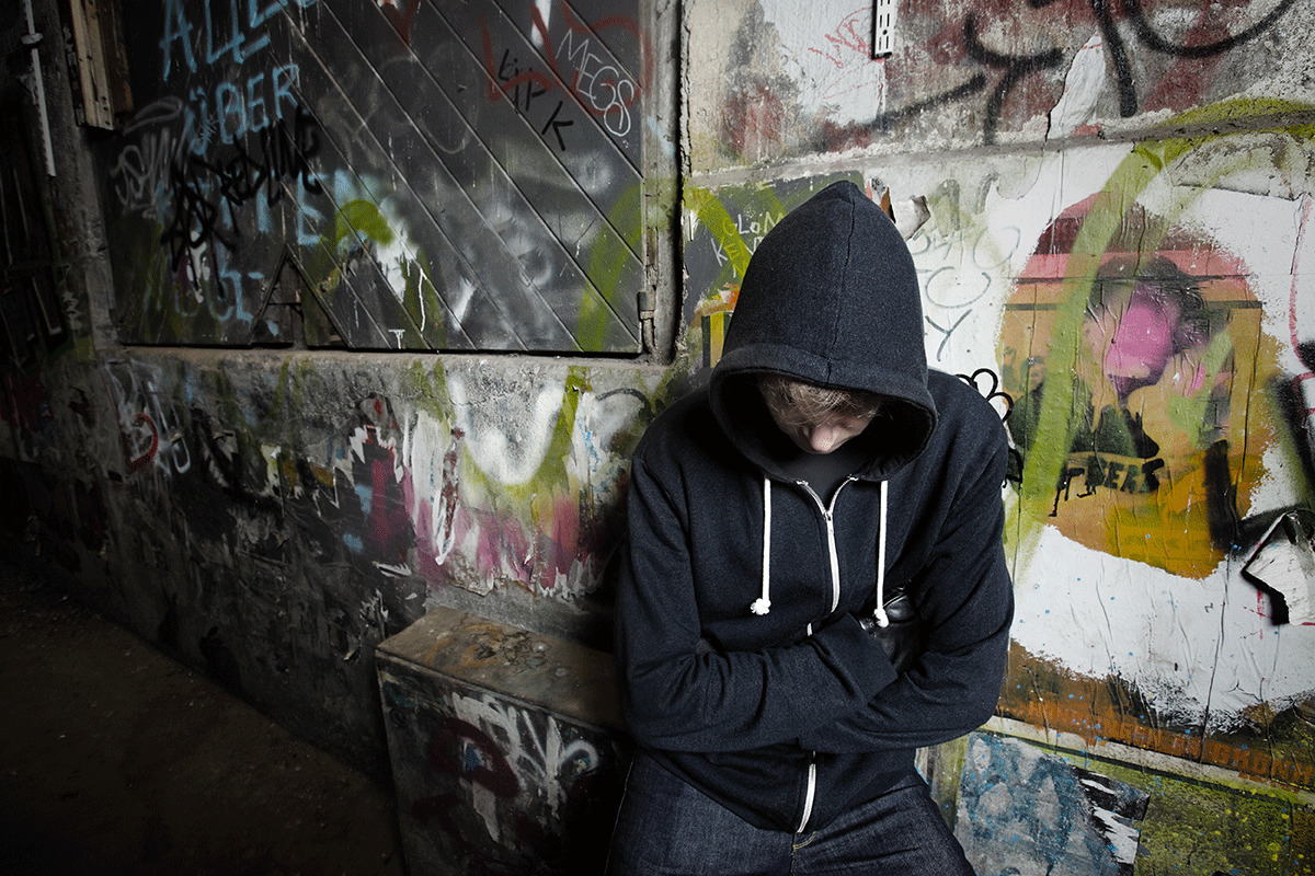 Man in hoodie leans against wall as he wonders what meth addiction looks like